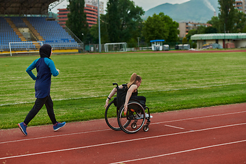 Image showing A Muslim woman in a burqa running together with a woman in a wheelchair on the marathon course, preparing for future competitions.