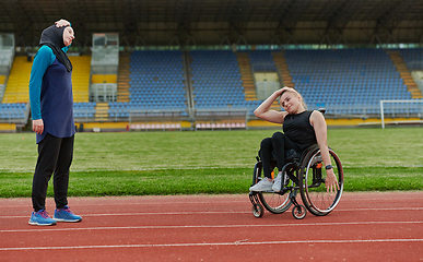 Image showing Two strong and inspiring women, one Muslim in a burka and the other in a wheelchair stretching necks while on the marathon course