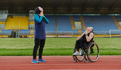 Image showing Two strong and inspiring women, one Muslim in a burka and the other in a wheelchair stretching necks while on the marathon course