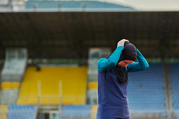 Image showing A Muslim woman in a burqa, an Islamic sports outfit, is doing body exercises, stretching her neck, legs and back after a hard training session on the marathon course.