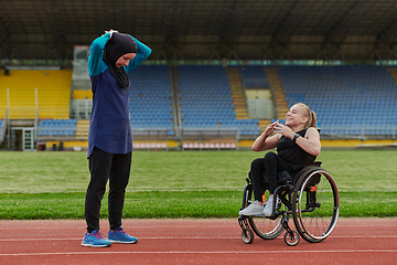 Image showing Two strong and inspiring women, one Muslim in a burka and the other in a wheelchair stretching necks while on the marathon course