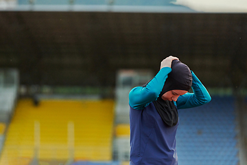 Image showing A Muslim woman in a burqa, an Islamic sports outfit, is doing body exercises, stretching her neck, legs and back after a hard training session on the marathon course.