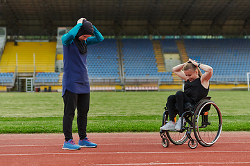 Image showing Two strong and inspiring women, one Muslim in a burka and the other in a wheelchair stretching necks while on the marathon course