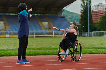 Image showing Two strong and inspiring women, one Muslim in a burka and the other in a wheelchair stretching necks while on the marathon course