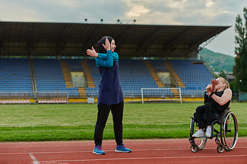 Image showing Two strong and inspiring women, one a Muslim wearing a burka and the other in a wheelchair stretching and preparing their bodies for a marathon race on the track