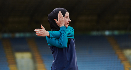 Image showing A Muslim woman in a burqa, an Islamic sports outfit, is doing body exercises, stretching her neck, legs and back after a hard training session on the marathon course.