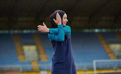 Image showing A Muslim woman in a burqa, an Islamic sports outfit, is doing body exercises, stretching her neck, legs and back after a hard training session on the marathon course.