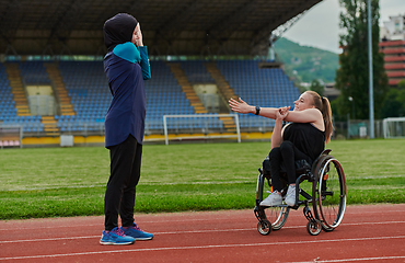 Image showing Two strong and inspiring women, one a Muslim wearing a burka and the other in a wheelchair stretching and preparing their bodies for a marathon race on the track