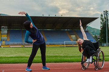 Image showing Two strong and inspiring women, one a Muslim wearing a burka and the other in a wheelchair stretching and preparing their bodies for a marathon race on the track