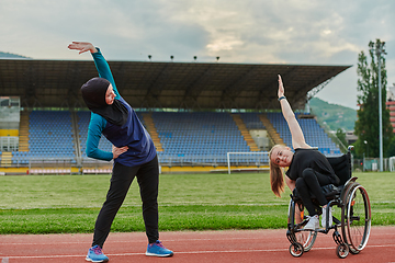 Image showing Two strong and inspiring women, one a Muslim wearing a burka and the other in a wheelchair stretching and preparing their bodies for a marathon race on the track