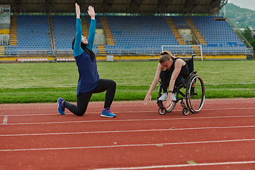 Image showing Two strong and inspiring women, one a Muslim wearing a burka and the other in a wheelchair stretching and preparing their bodies for a marathon race on the track