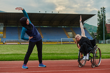 Image showing Two strong and inspiring women, one a Muslim wearing a burka and the other in a wheelchair stretching and preparing their bodies for a marathon race on the track