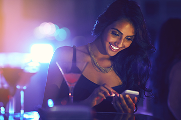 Image showing Get here now, this party is great. Shot of a woman using her cellphone while sitting at a table in a nightclub.