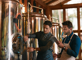 Image showing Lets hope this batch is a good one. Shot of two young working men doing inspection of their beer making machinery inside of a beer brewery during the day.