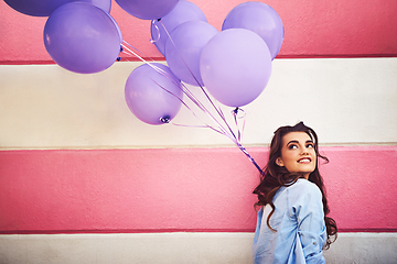 Image showing Having colourful fun in the city. Cropped shot of a beautiful young woman holding purple balloons against a wall outside.