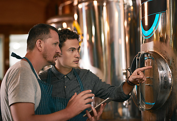 Image showing Is this container cold enough. Shot of two young working men doing inspection of their beer making machinery inside of a beer brewery during the day.