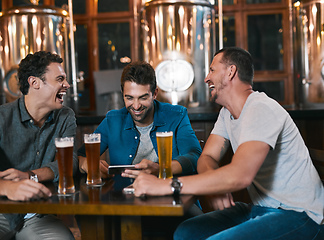 Image showing Time to talk business over a beer. Shot of three cheerful young men drinking beer together at a table inside of a beer brewery during the day.