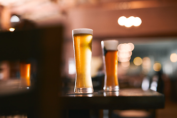 Image showing Take the load of with a glass of beer. Shot of two glasses of beer standing on its own at a table inside of a beer brewery during the day.