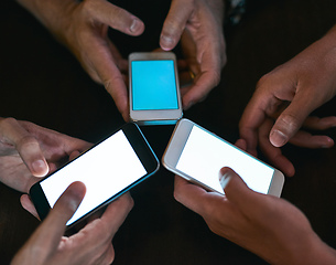 Image showing All for one and one for all. High angle shot of three unrecognizable people seated in a circle at a table while browsing on their cellphones.