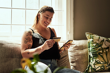 Image showing Shopping day minus the queues. Shot of a young woman using a smartphone and credit card on the sofa at home.