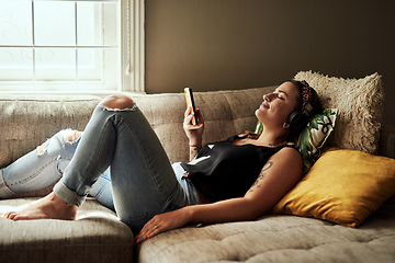 Image showing When words are few music says a lot. Shot of a young woman using a smartphone and headphones on the sofa at home.