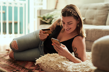 Image showing Shopping just gets easier and easier. Shot of a young woman using a smartphone and credit card in her living room at home.