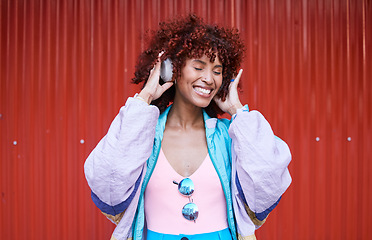 Image showing Music, dance and headphones with a retro woman on a red background in the city for energy or freedom. Radio, smile and streaming audio with a happy young afro person listening to sound for wellness