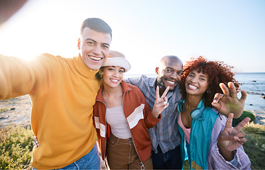 Image showing Selfie, happy and portrait of friends by the beach on summer vacation, adventure or weekend trip. Smile, diversity and young people having fun and taking picture with peace sign by ocean on holiday.