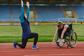 Image showing Two strong and inspiring women, one a Muslim wearing a burka and the other in a wheelchair stretching and preparing their bodies for a marathon race on the track