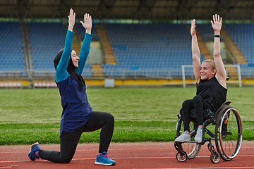 Image showing Two strong and inspiring women, one a Muslim wearing a burka and the other in a wheelchair stretching and preparing their bodies for a marathon race on the track