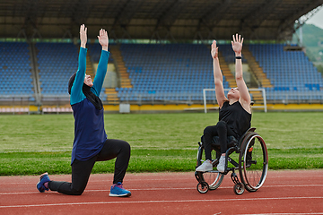 Image showing Two strong and inspiring women, one a Muslim wearing a burka and the other in a wheelchair stretching and preparing their bodies for a marathon race on the track