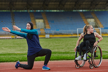 Image showing Two strong and inspiring women, one a Muslim wearing a burka and the other in a wheelchair stretching and preparing their bodies for a marathon race on the track