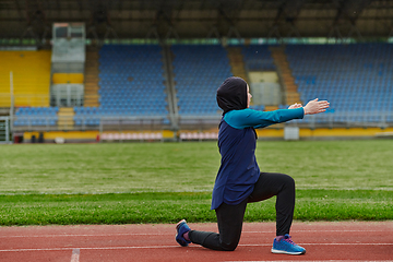 Image showing A Muslim woman in a burqa, an Islamic sports outfit, is doing body exercises, stretching her neck, legs and back after a hard training session on the marathon course.