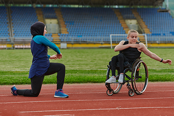 Image showing Two strong and inspiring women, one a Muslim wearing a burka and the other in a wheelchair stretching and preparing their bodies for a marathon race on the track