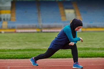 Image showing A Muslim woman in a burqa, an Islamic sports outfit, is doing body exercises, stretching her neck, legs and back after a hard training session on the marathon course.