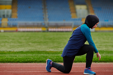 Image showing A Muslim woman in a burqa, an Islamic sports outfit, is doing body exercises, stretching her neck, legs and back after a hard training session on the marathon course.