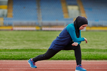 Image showing A Muslim woman in a burqa, an Islamic sports outfit, is doing body exercises, stretching her neck, legs and back after a hard training session on the marathon course.