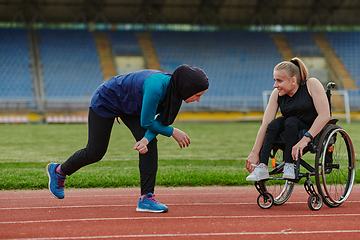 Image showing Two strong and inspiring women, one a Muslim wearing a burka and the other in a wheelchair stretching and preparing their bodies for a marathon race on the track