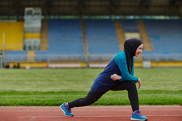 Image showing A Muslim woman in a burqa, an Islamic sports outfit, is doing body exercises, stretching her neck, legs and back after a hard training session on the marathon course.