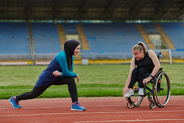 Image showing Two strong and inspiring women, one a Muslim wearing a burka and the other in a wheelchair stretching and preparing their bodies for a marathon race on the track