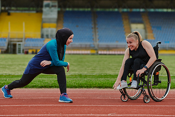 Image showing Two strong and inspiring women, one a Muslim wearing a burka and the other in a wheelchair stretching and preparing their bodies for a marathon race on the track