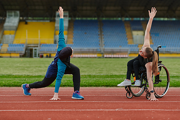 Image showing Two strong and inspiring women, one a Muslim wearing a burka and the other in a wheelchair stretching and preparing their bodies for a marathon race on the track