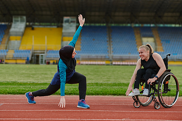 Image showing Two strong and inspiring women, one a Muslim wearing a burka and the other in a wheelchair stretching and preparing their bodies for a marathon race on the track