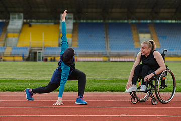 Image showing Two strong and inspiring women, one a Muslim wearing a burka and the other in a wheelchair stretching and preparing their bodies for a marathon race on the track