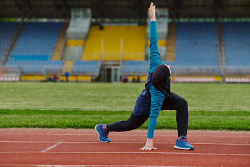 Image showing A Muslim woman in a burqa, an Islamic sports outfit, is doing body exercises, stretching her neck, legs and back after a hard training session on the marathon course.