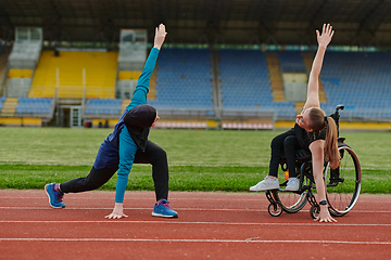 Image showing Two strong and inspiring women, one a Muslim wearing a burka and the other in a wheelchair stretching and preparing their bodies for a marathon race on the track