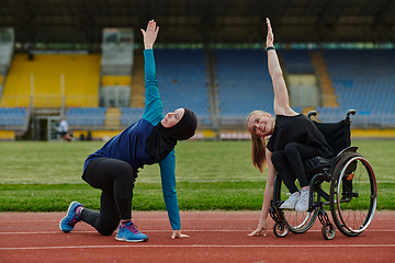 Image showing Two strong and inspiring women, one a Muslim wearing a burka and the other in a wheelchair stretching and preparing their bodies for a marathon race on the track