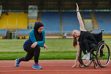 Image showing Two strong and inspiring women, one a Muslim wearing a burka and the other in a wheelchair stretching and preparing their bodies for a marathon race on the track