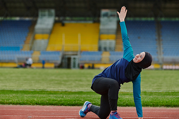 Image showing A Muslim woman in a burqa, an Islamic sports outfit, is doing body exercises, stretching her neck, legs and back after a hard training session on the marathon course.