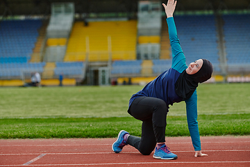 Image showing A Muslim woman in a burqa, an Islamic sports outfit, is doing body exercises, stretching her neck, legs and back after a hard training session on the marathon course.